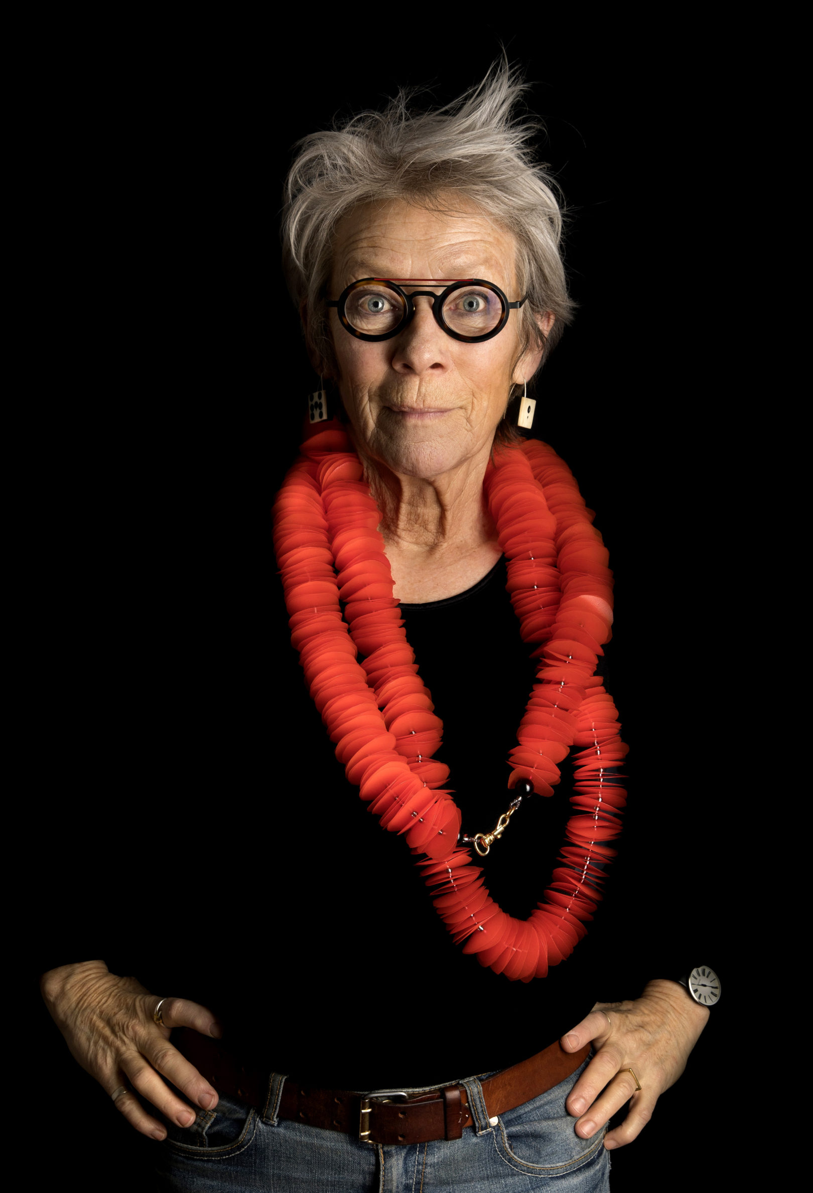 Kirsten Sonne photographed against a black background wearing a large red necklace made from many plastic disks.