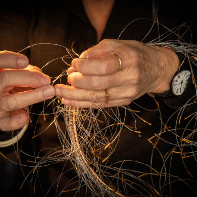 Kirsten Sonne's hands with a large bundle of copper wire around her wrists. She is weaving the stands together.