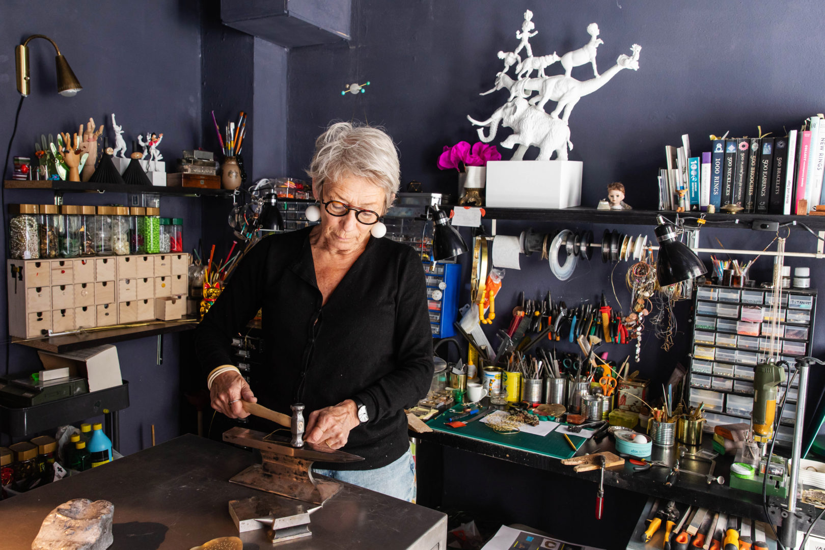 Sonne, wearing all black, working in her studio. Hammering silver on an anvil.