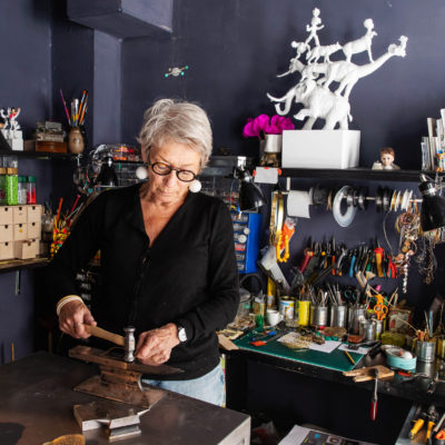 Sonne, wearing all black, working in her studio. Hammering silver on an anvil.