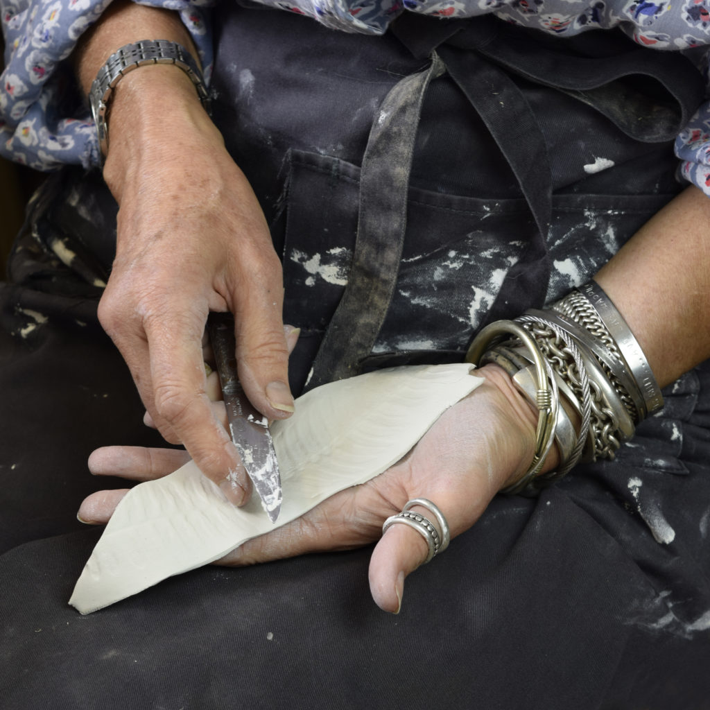 A pair of hands moulding a porcelain fish