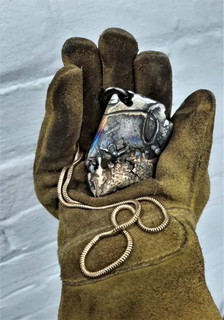 Gloved hand holding scrap metal pendant